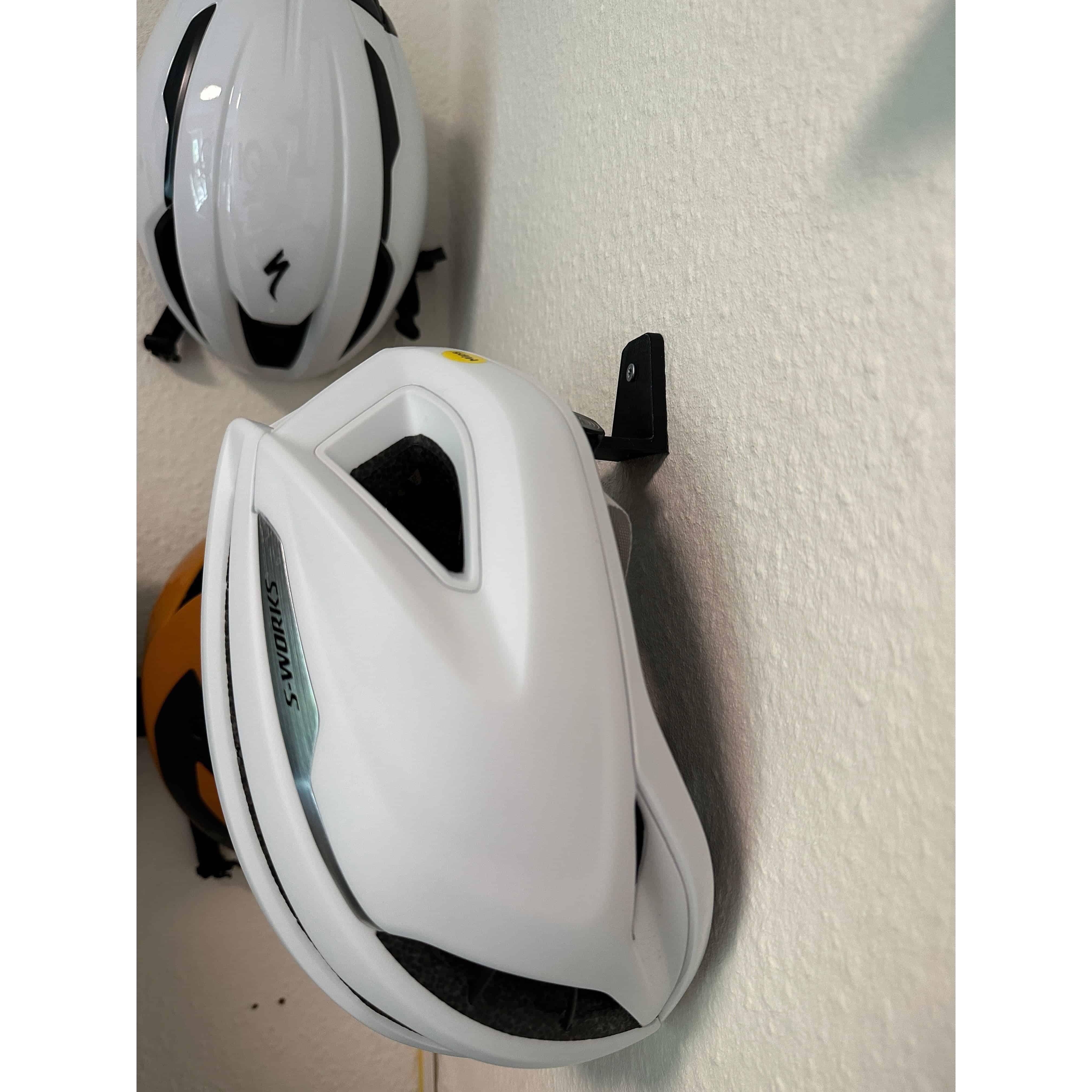 Two cycling helmets stored on wall mounted helmet hangers, Specialized road helmets