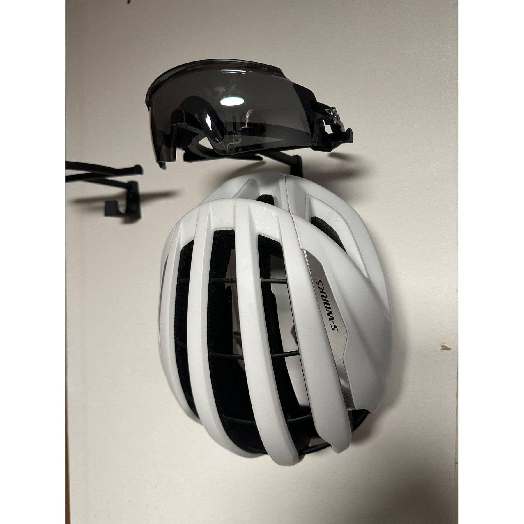Wall mounted helmet and glasses hanger holding white road cycling helmet and sunglasses