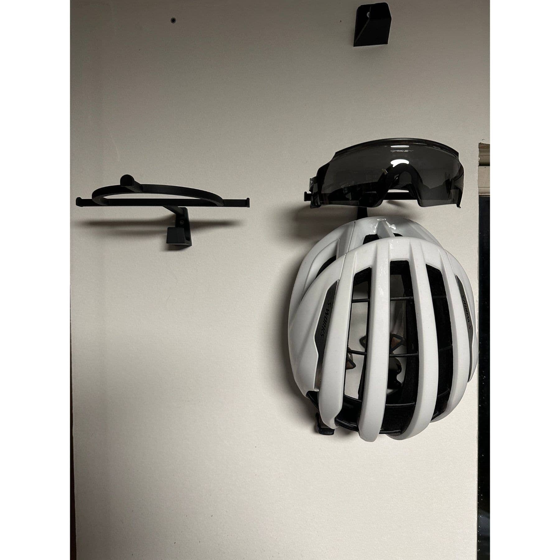 Wall mounted hanger holding white cycling helmet and glasses for organized gear storage