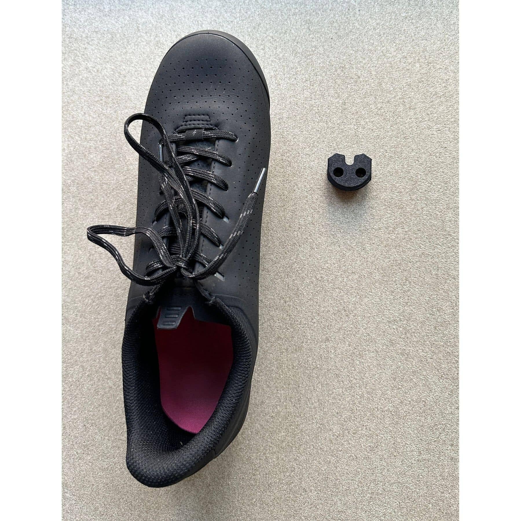 Black road cycling shoe next to wall mounted shoe holder with cleat slot